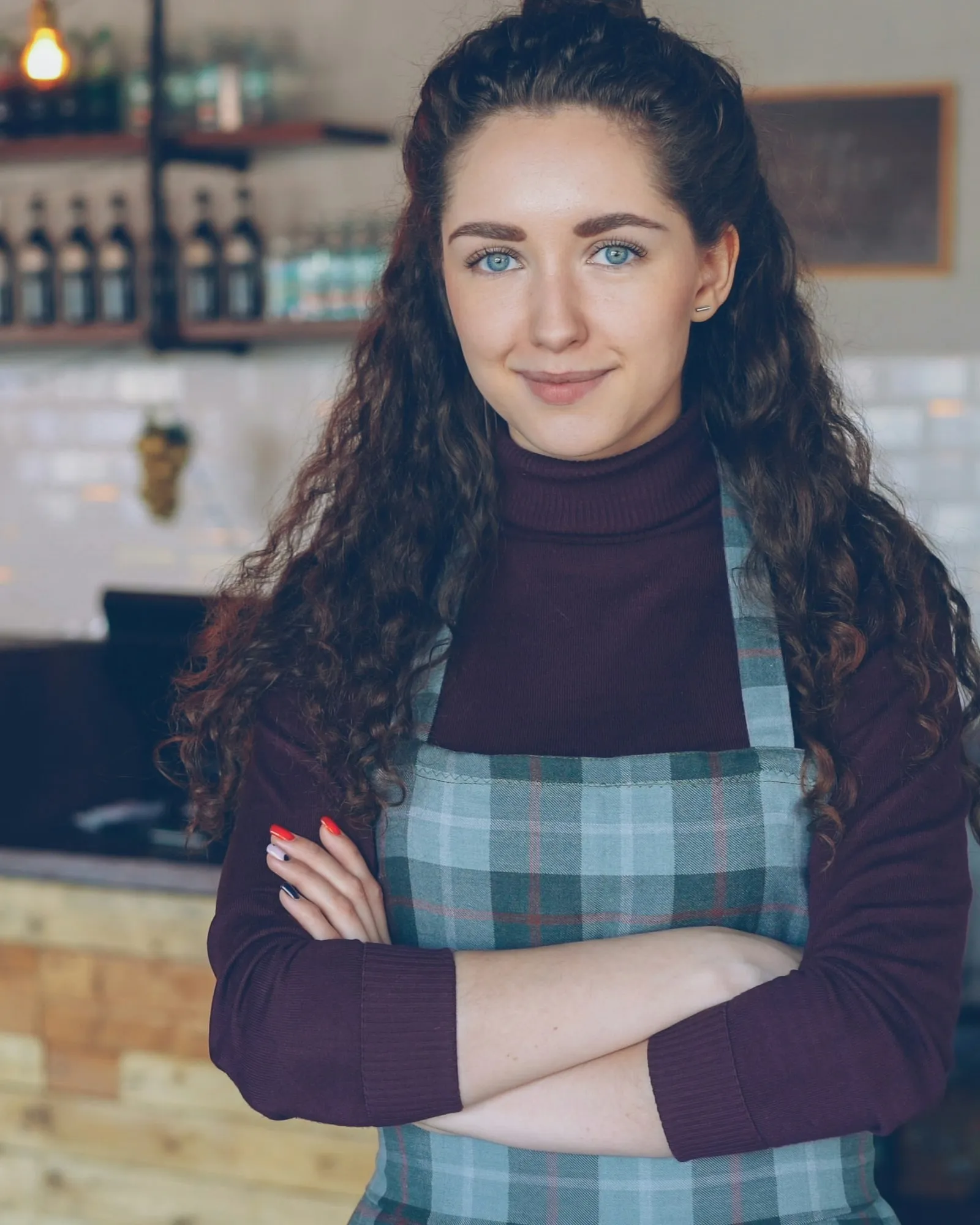 Smiling café owner with her arms folded, standing in her coffee shop