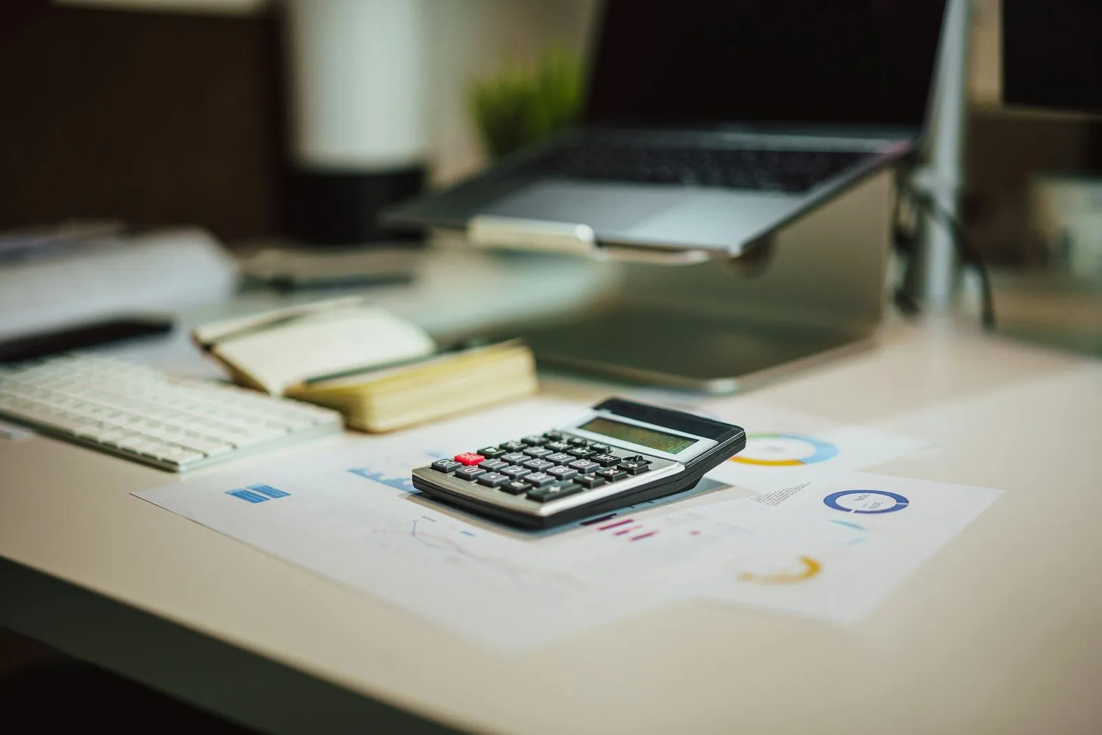 Calculator, notebook and paperwork on a desk in front of a laptop while the month's cash flow is worked through